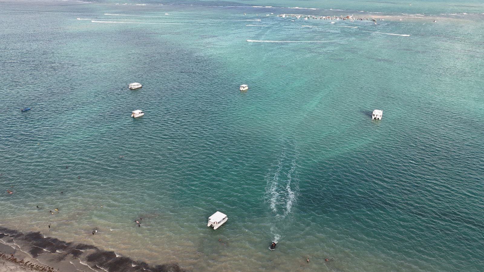 Vista aérea do mar verde-azulado em Camboinha, com catamarãs a caminho de Areia Vermelha